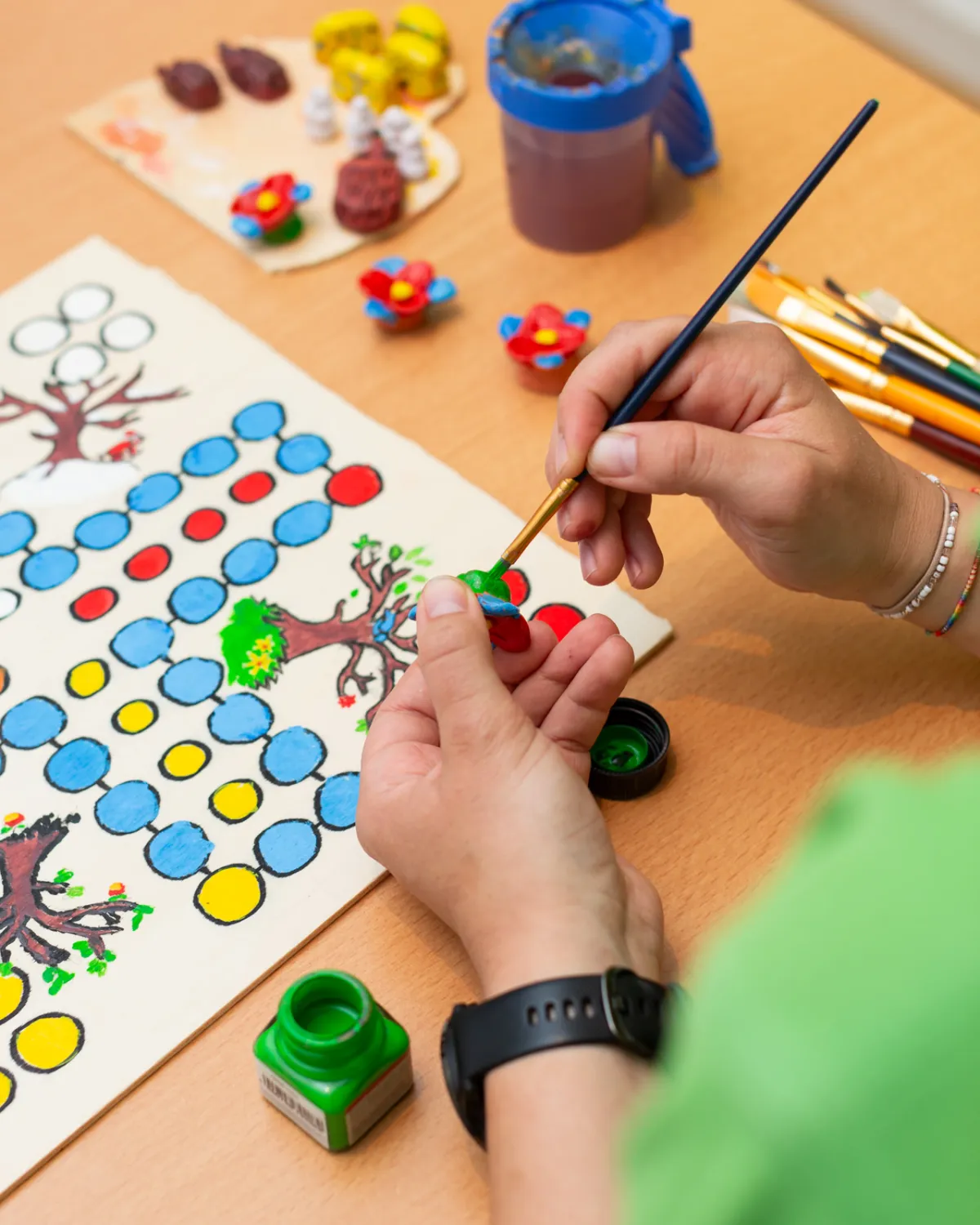 Hände malen mit einem Pinsel ein Spielfeld aus, daneben Steckfiguren