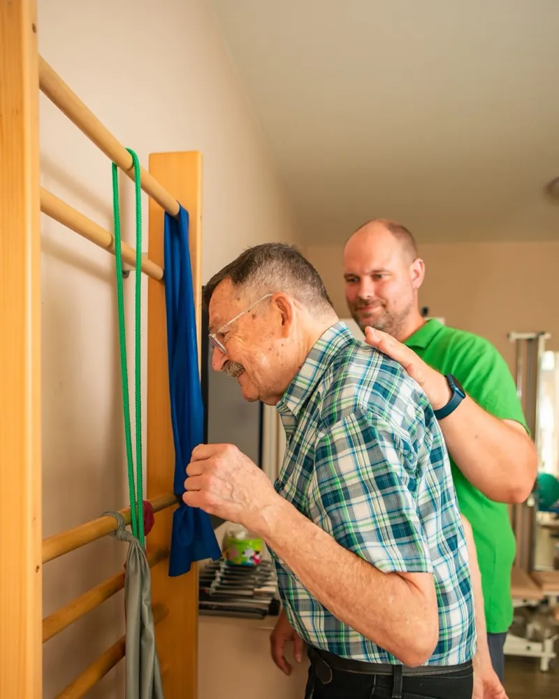Ein Therapeut korrigiert die Haltung eines Patienten an der Sprossenwand