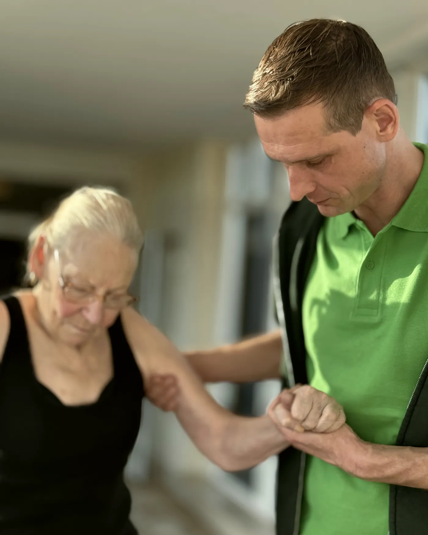 Therapeut führt eine ältere Frau am Arm beim Gehen